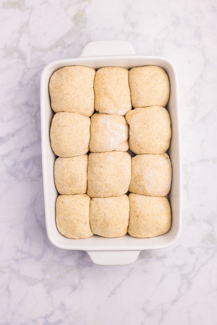 "Twelve risen dough balls arranged snugly in a white baking dish, ready to bake.