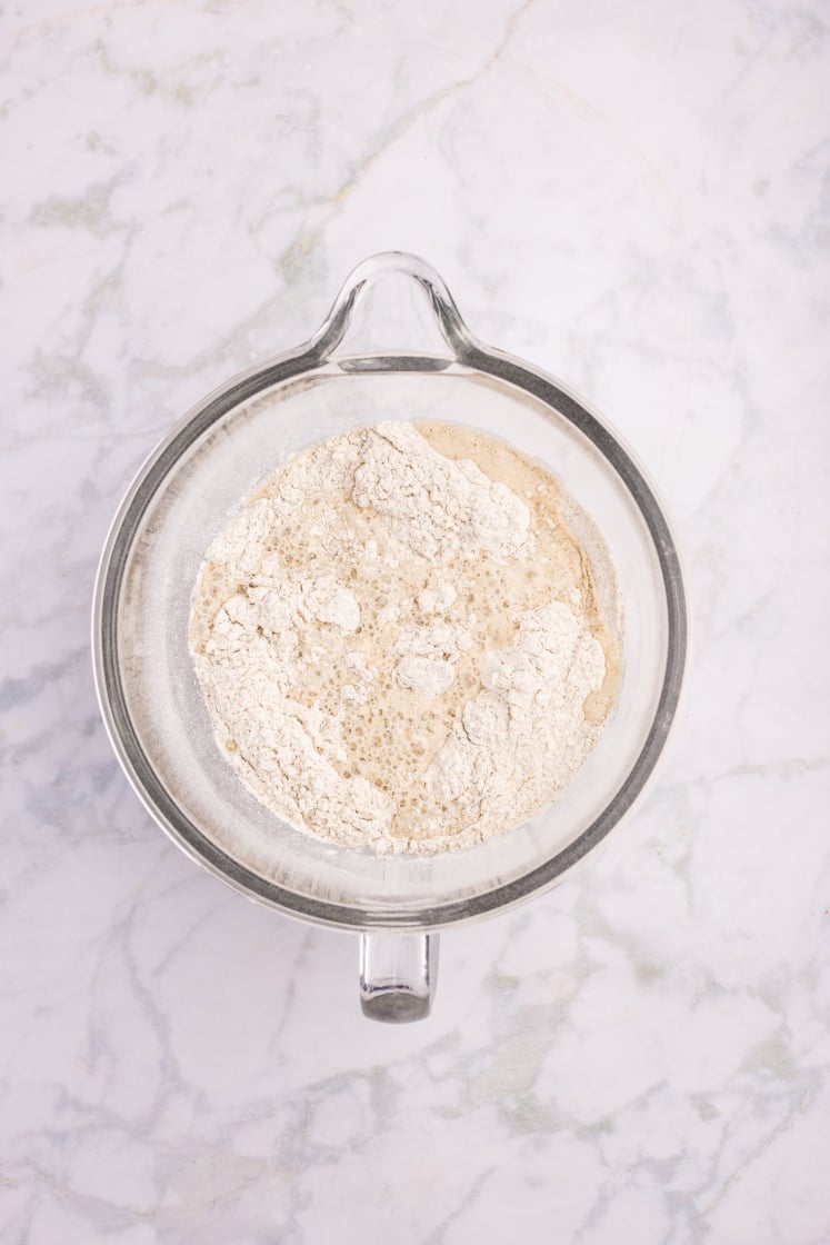 Glass mixing bowl with flour mixture and warm milk mixture beginning to combine.