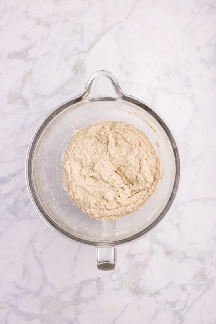 Glass mixing bowl with freshly mixed rye dinner roll dough, appearing soft and slightly sticky.