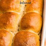 A white baking dish filled with golden-brown rye dinner rolls, arranged closely together.