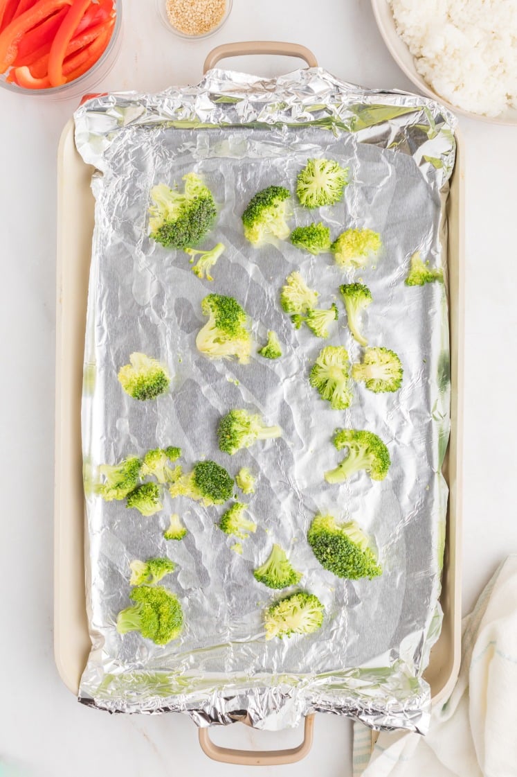Broccoli florets arranged on a foil-lined sheet pan before roasting.