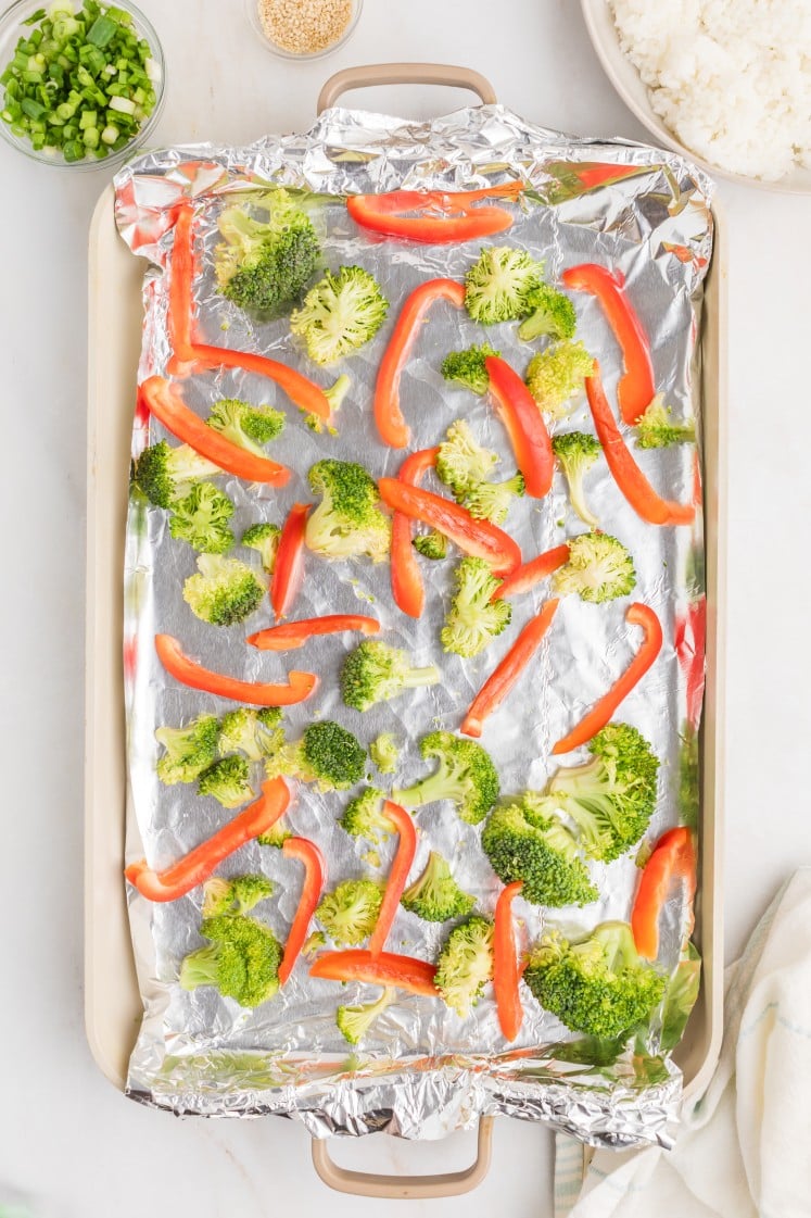 Broccoli and red bell peppers on a foil-lined sheet pan.