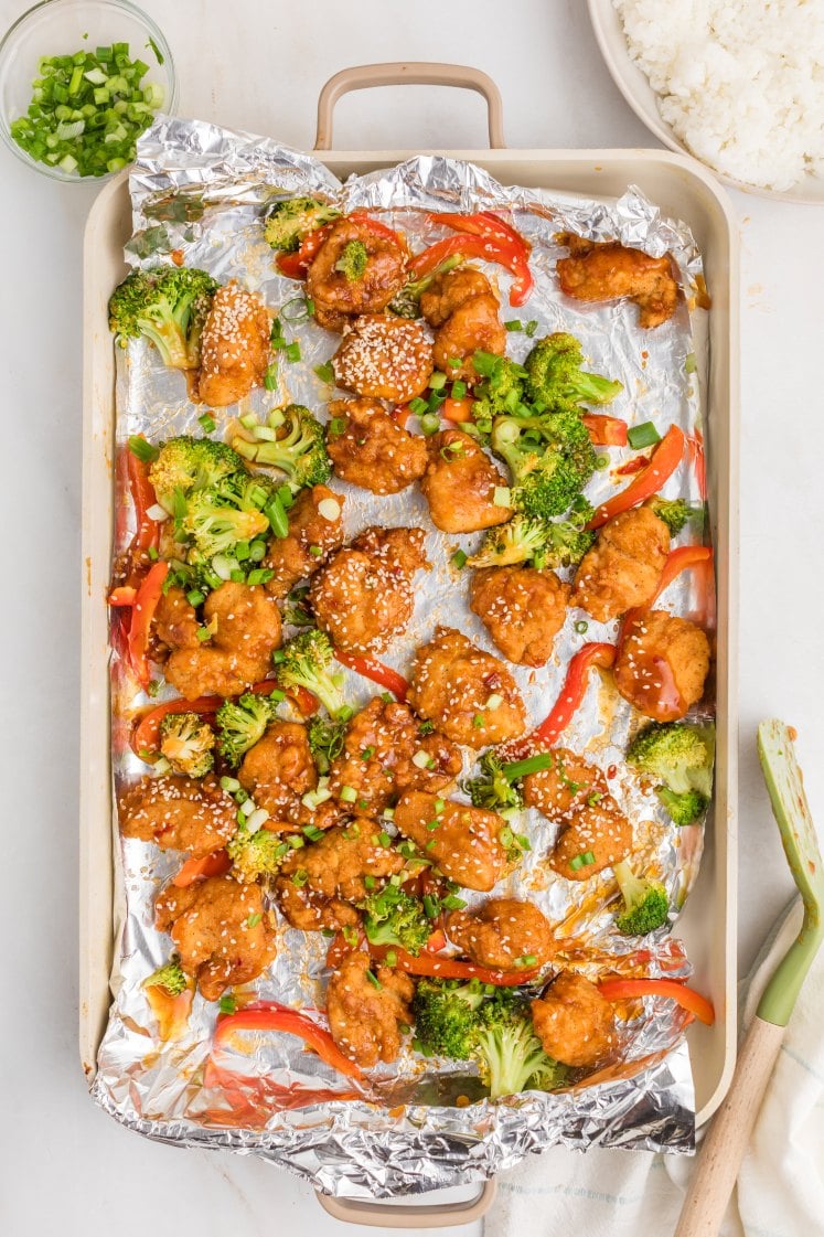 Sheet-pan general tso’s chicken topped with sesame seeds and green onions on a.