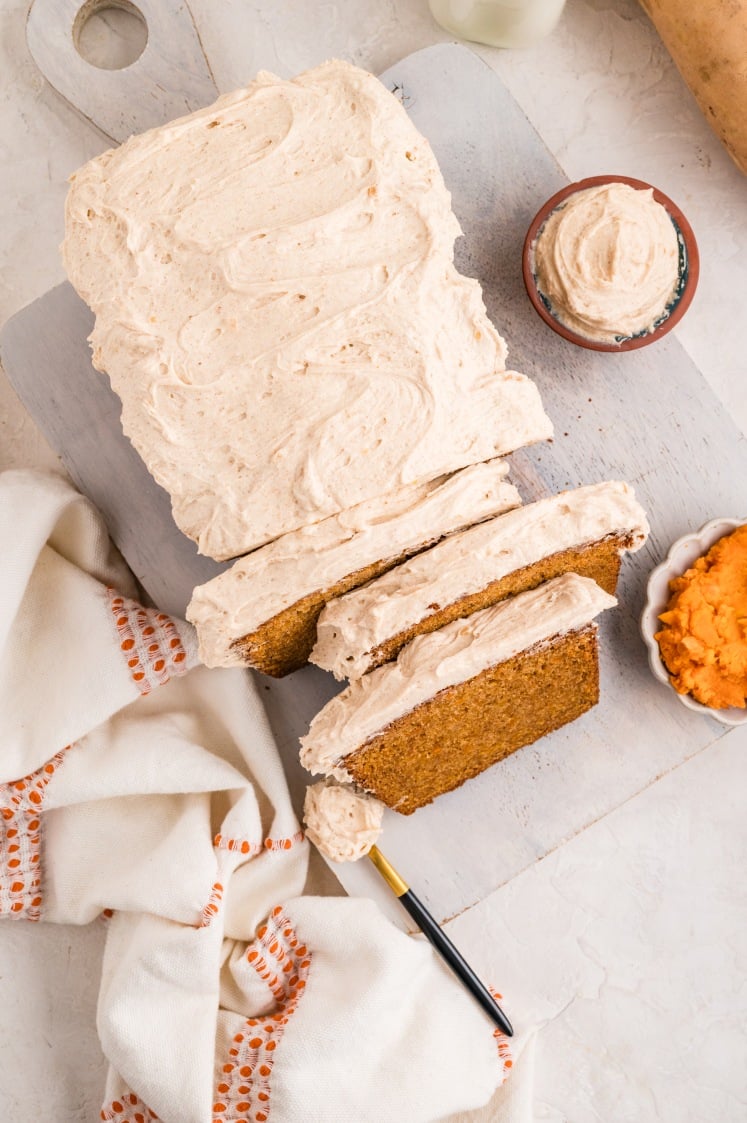 Sliced sweet potato loaf with creamy frosting on a cutting board.