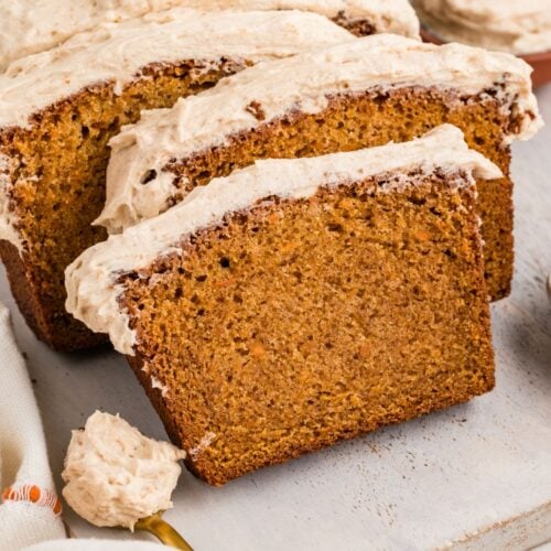 Sliced sweet potato loaf topped with creamy frosting on a cutting board.