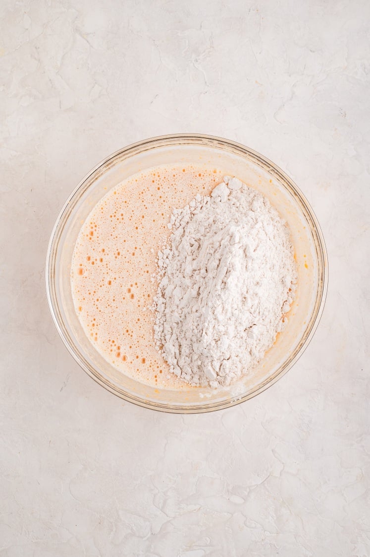 Dry ingredients added to the wet ingredients in a glass bowl.