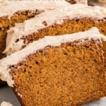 Sliced sweet potato bread topped with browned butter cream cheese frosting, displayed on a light surface with a serving of frosting nearby.