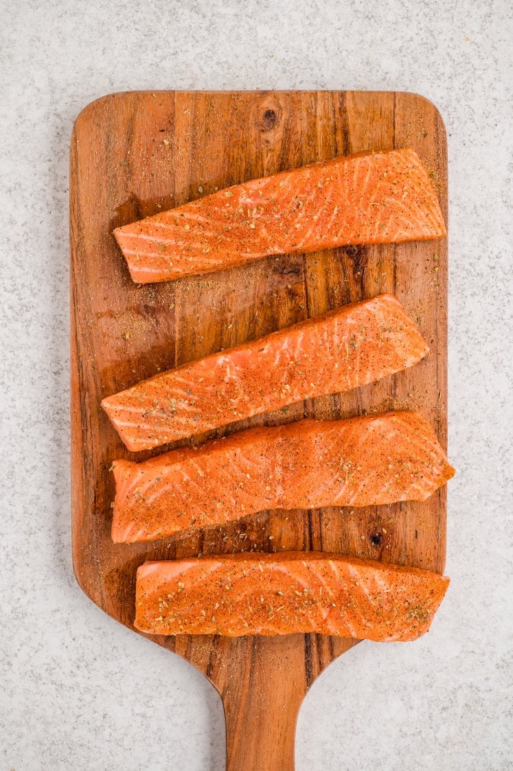 Seasoned raw salmon fillets on a wooden cutting board.