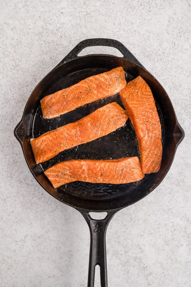 Seasoned salmon fillets cooking in a skillet.