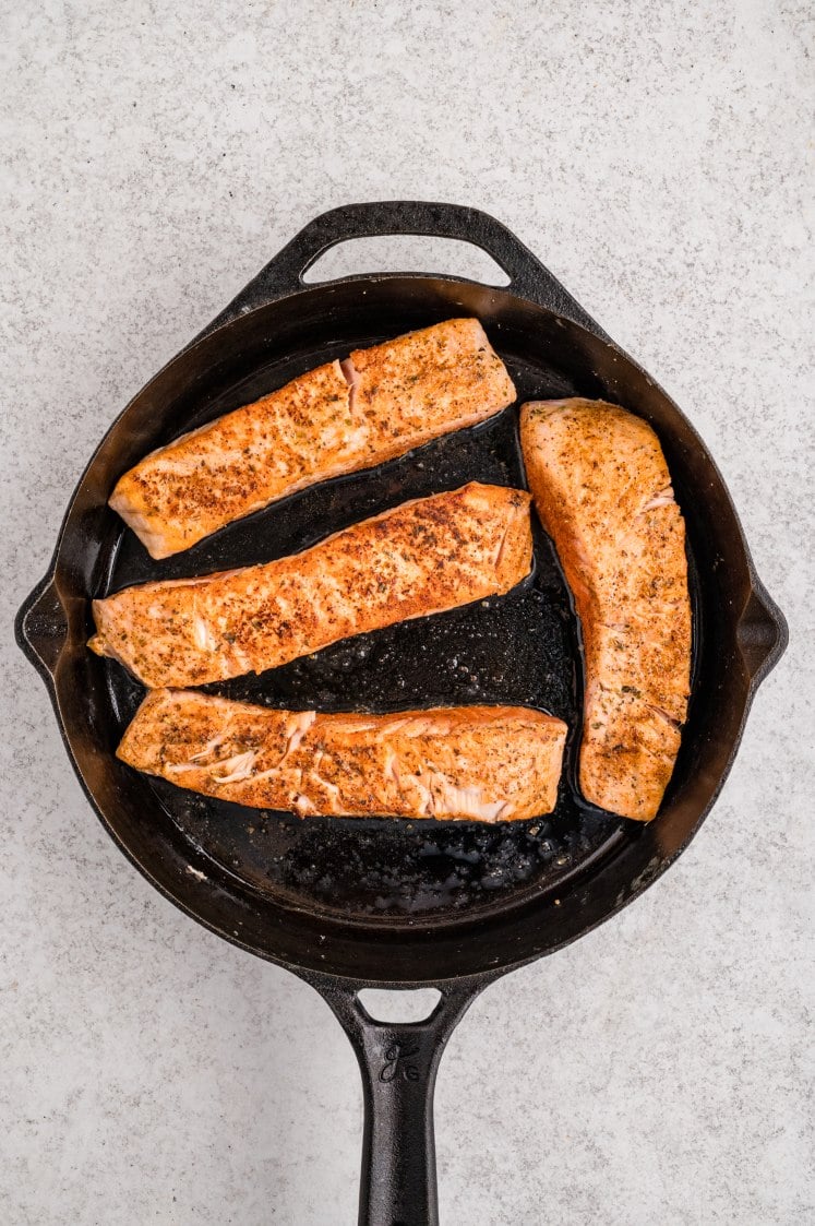 Cajun-seasoned salmon fillets searing in a skillet.