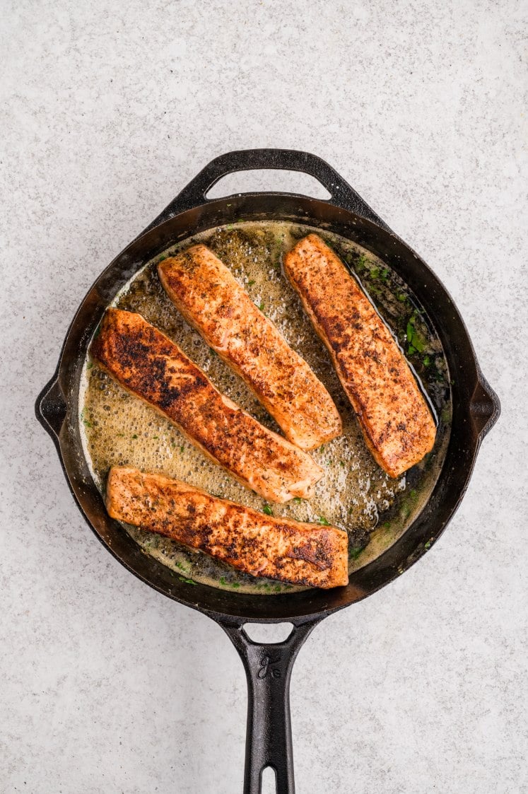 Cajun salmon fillets cooking in garlic butter sauce.