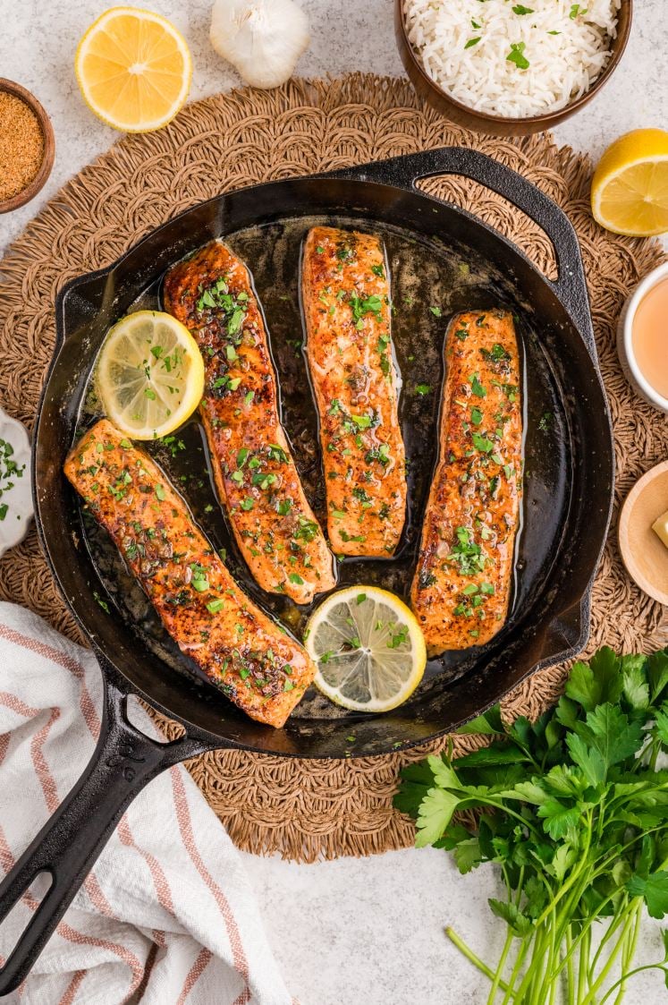Cajun salmon fillets finished in a skillet with lemon and herbs.