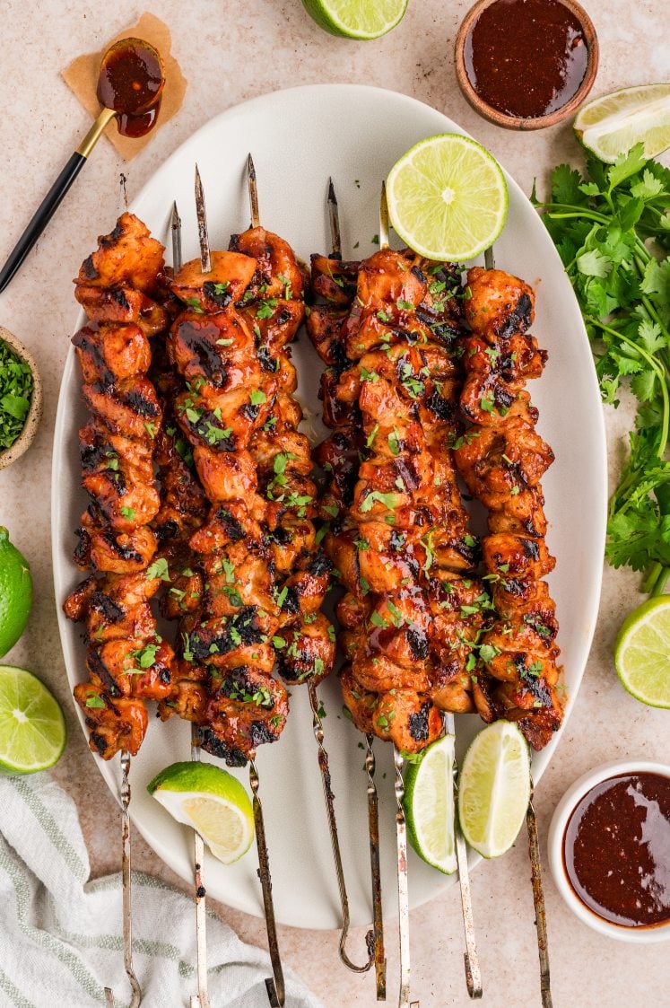 Grilled chipotle chicken skewers garnished with cilantro and lime wedges.