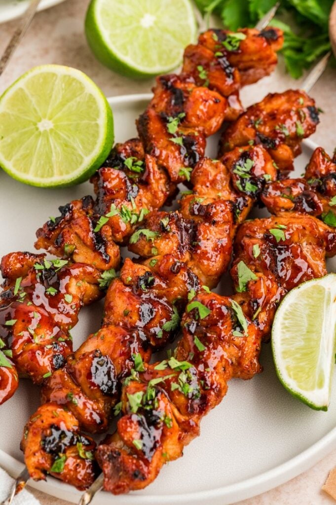 Chipotle chicken skewers glazed with sauce, garnished with cilantro, served with lime wedges.