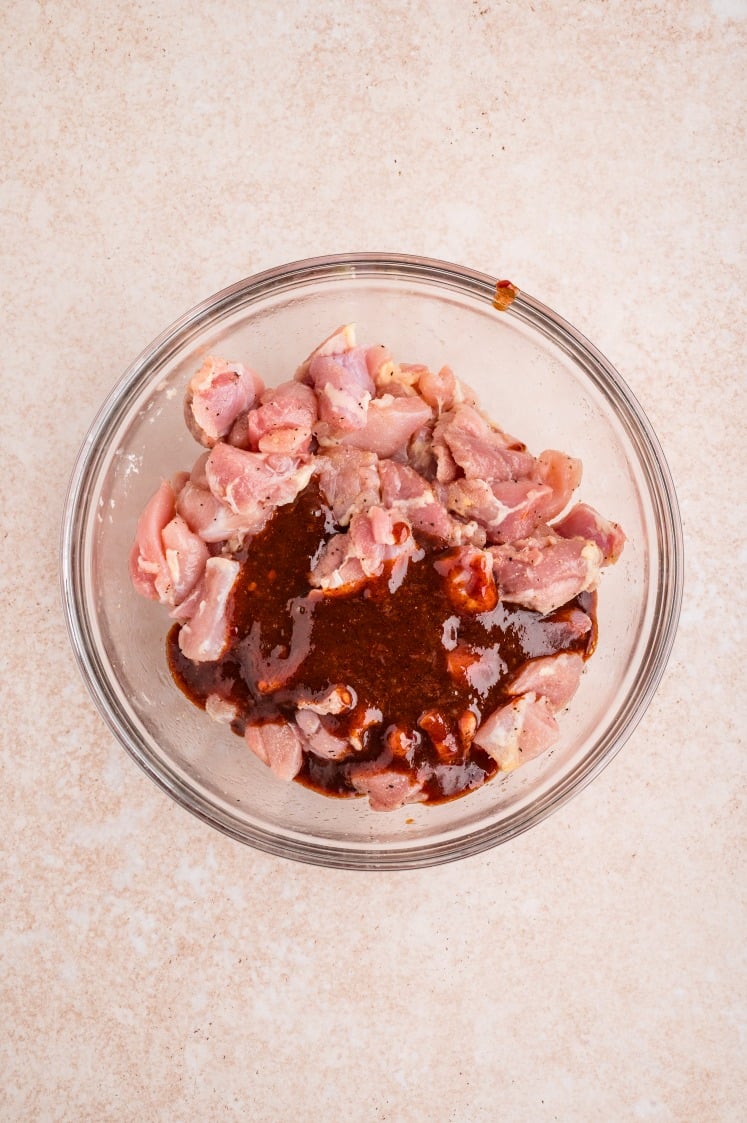 Raw chicken mixed with chipotle marinade in a glass bowl.