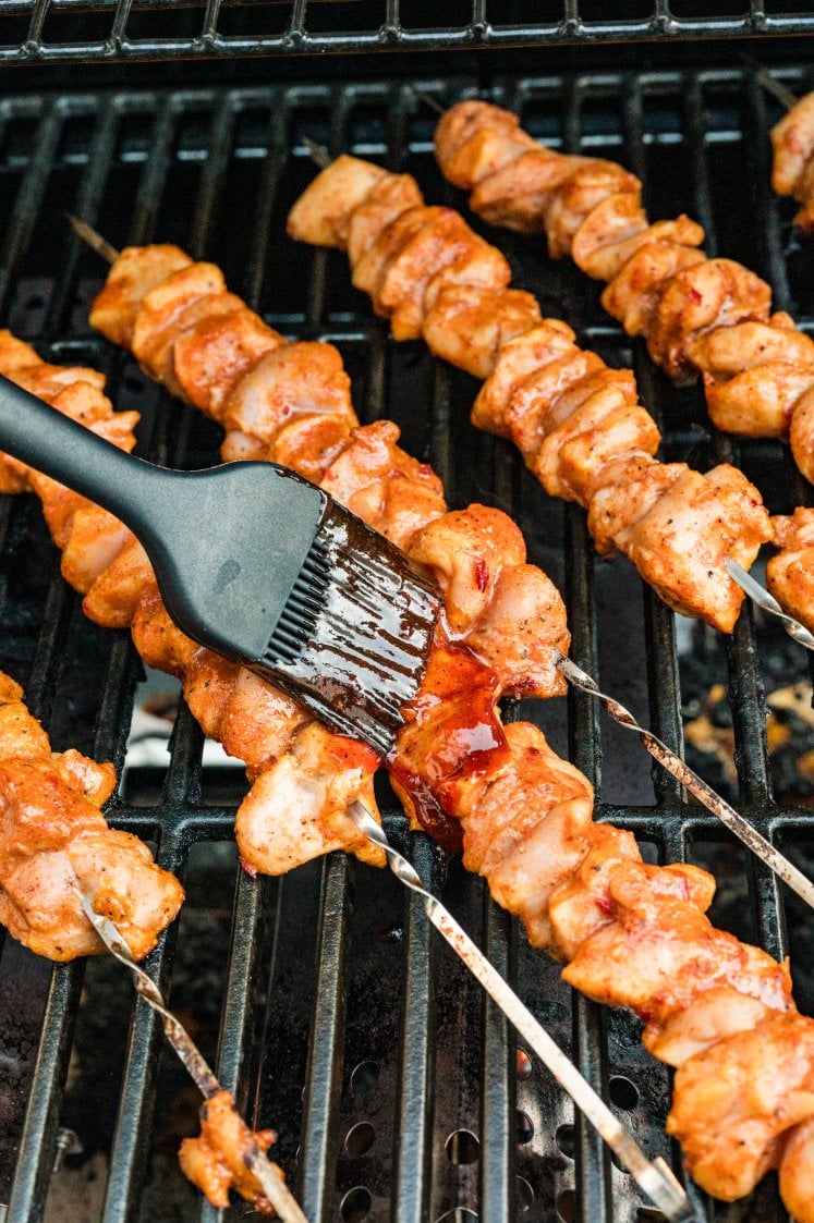 Chipotle chicken skewers being brushed with sauce on the grill.