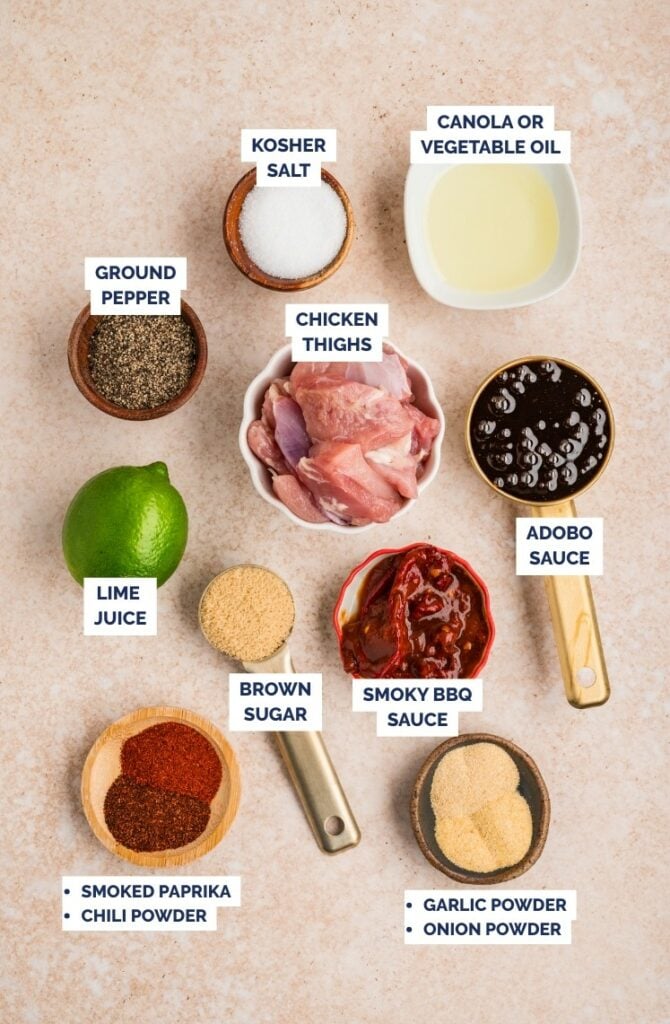Ingredients for chipotle chicken skewers laid out on a surface, including chicken thighs, spices, sauces, oil, and lime.