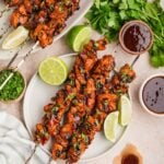 Chipotle chicken skewers on plates with lime wedges, cilantro, and dipping sauce.