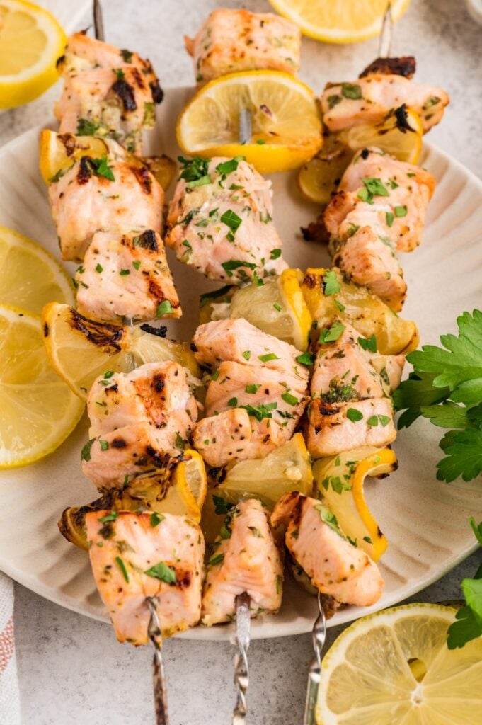 Lemon garlic salmon skewers served on a platter with charred lemon slices and fresh herbs, lightly grilled and finished with a squeeze of citrus.