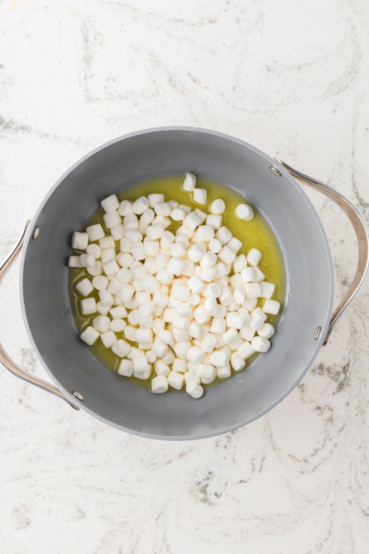 Mini marshmallows melting in butter in a saucepan.