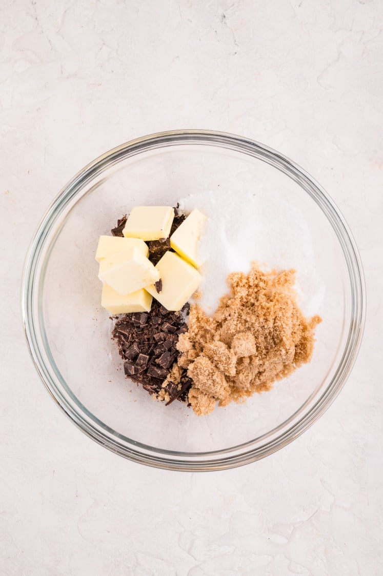 Butter, chopped chocolate, granulated sugar, and brown sugar in a mixing bowl, ready to be melted together.