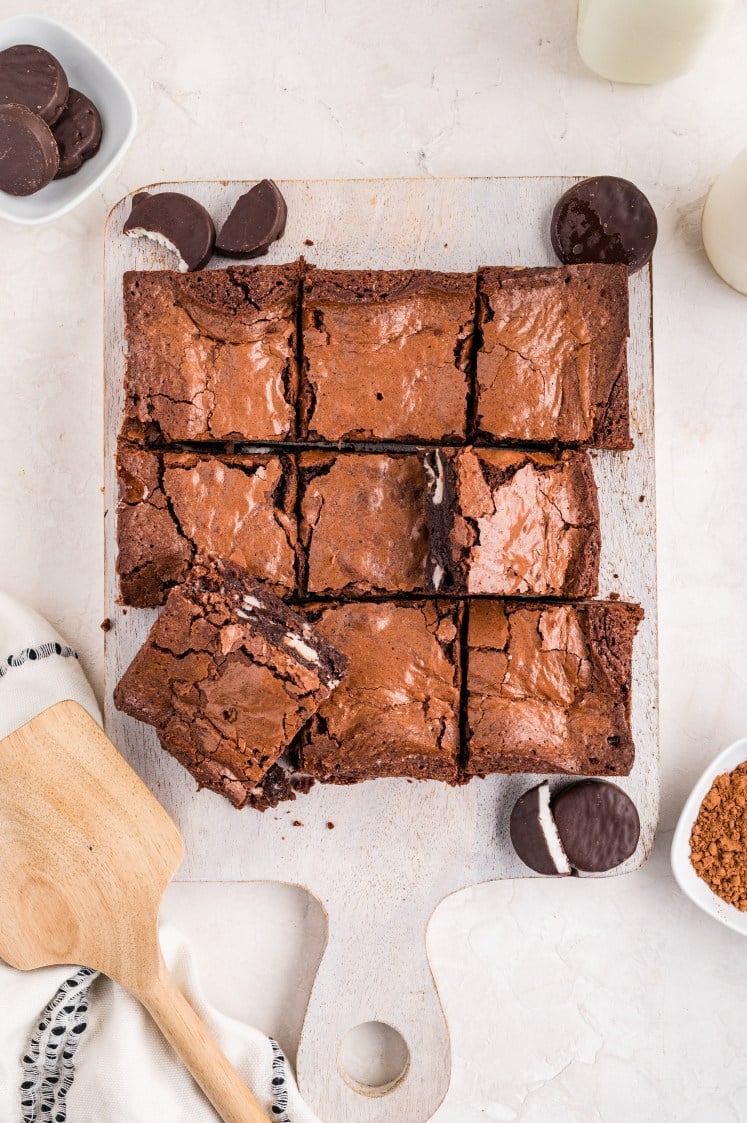 Freshly sliced peppermint patty brownies arranged on a cutting board, showing crackly tops, fudgy centers, and pockets of minty filling throughout.
