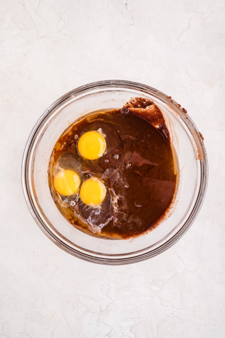Eggs added to the melted chocolate and sugar mixture in a glass bowl, ready to be whisked until smooth.
