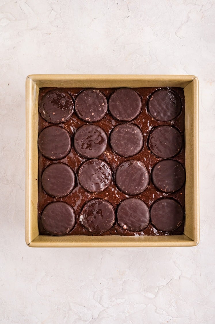 Mini peppermint patties arranged evenly over the brownie batter, gently pressed in so they melt into a gooey mint layer while baking.