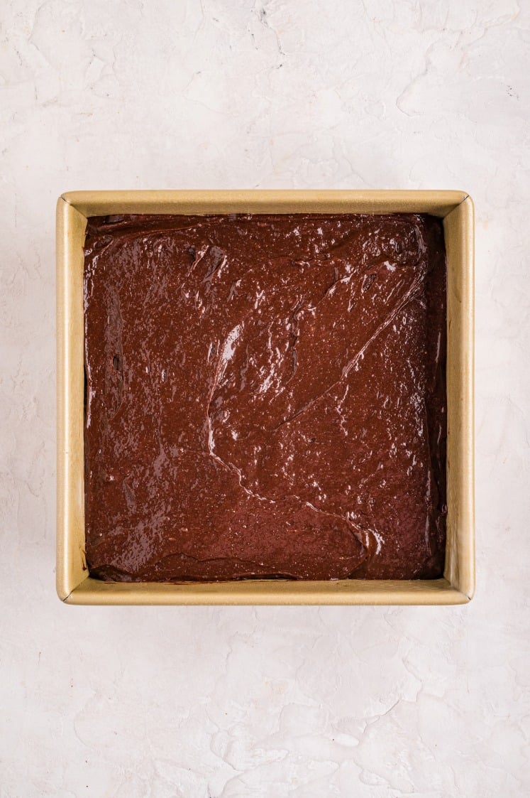 The brownie batter smoothed back over the peppermint patties, sealing them inside for a rich, fudgy brownie with a hidden minty center once baked.