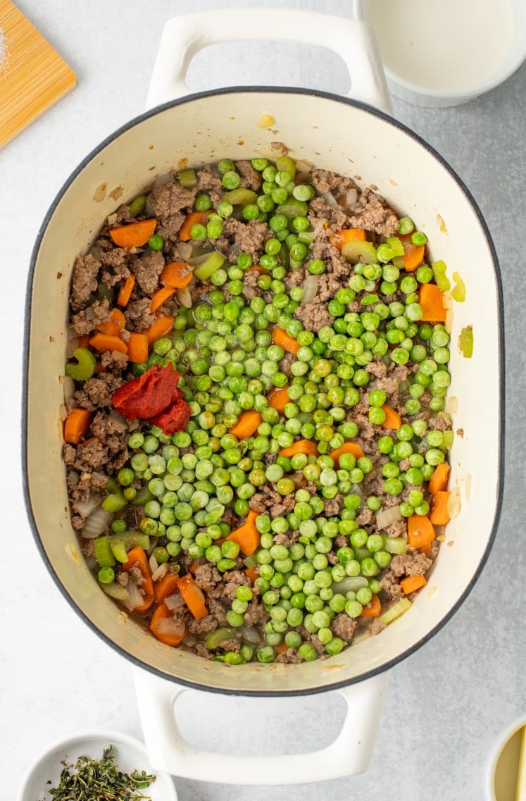 Cooked ground beef mixed with onions, carrots, and celery, topped with peas and tomato paste just before stirring everything together.
