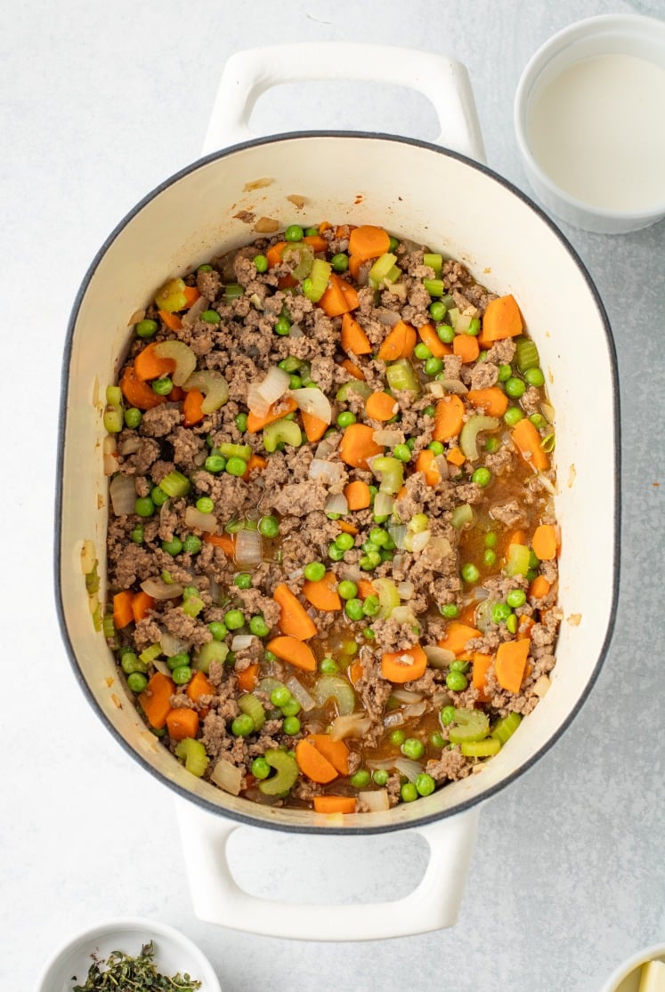 The beef and vegetables are fully mixed and simmering in broth, creating a savory filling with tender carrots, celery, onions, and peas evenly coated in sauce.