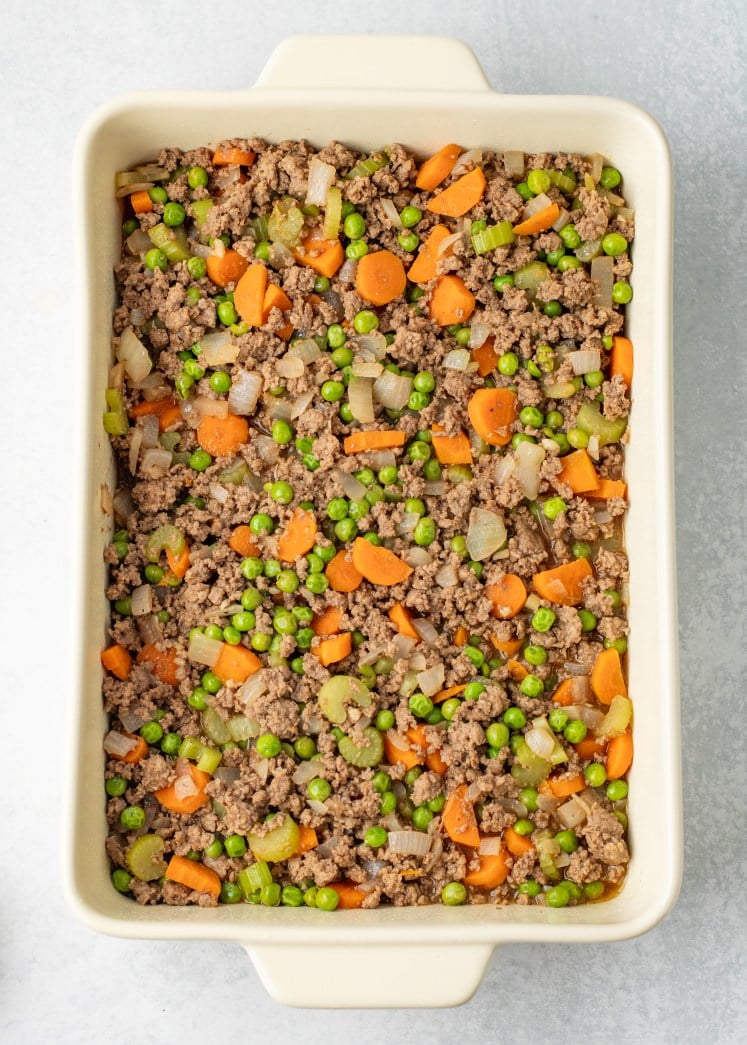 The beef and vegetable mixture is spread evenly into the baking dish, forming a hearty base with plenty of carrots, peas, and onions in every bite.