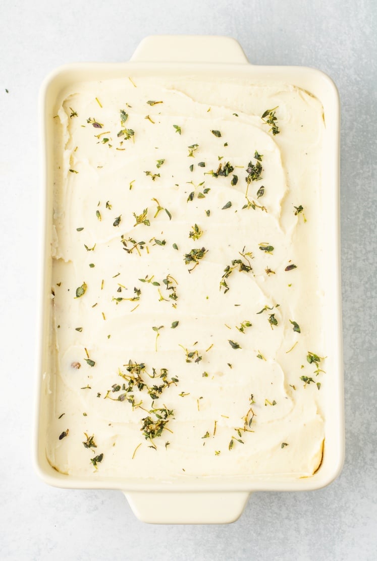 The mashed potatoes are spread over the filling in an even layer, then finished with a light sprinkle of thyme so it’s ready for the oven and that golden top.