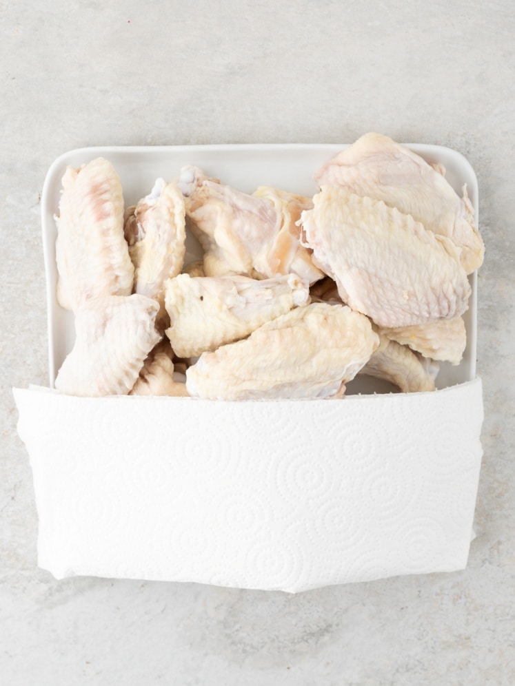 Raw chicken wings on a tray lined with paper towels.
