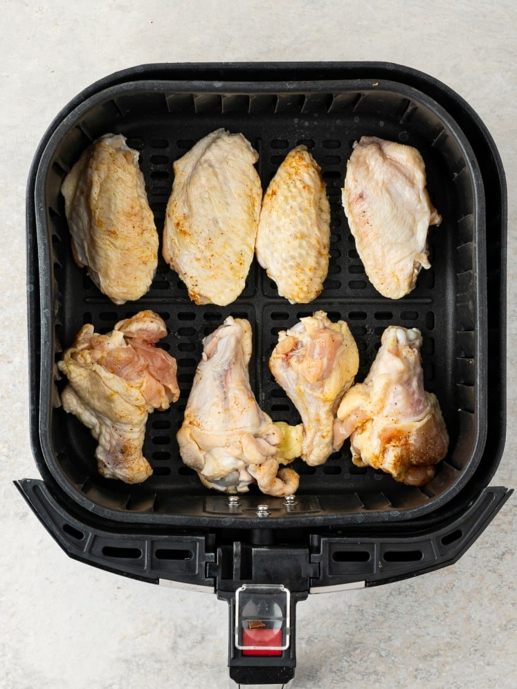 Raw seasoned chicken wings arranged in an air fryer basket.