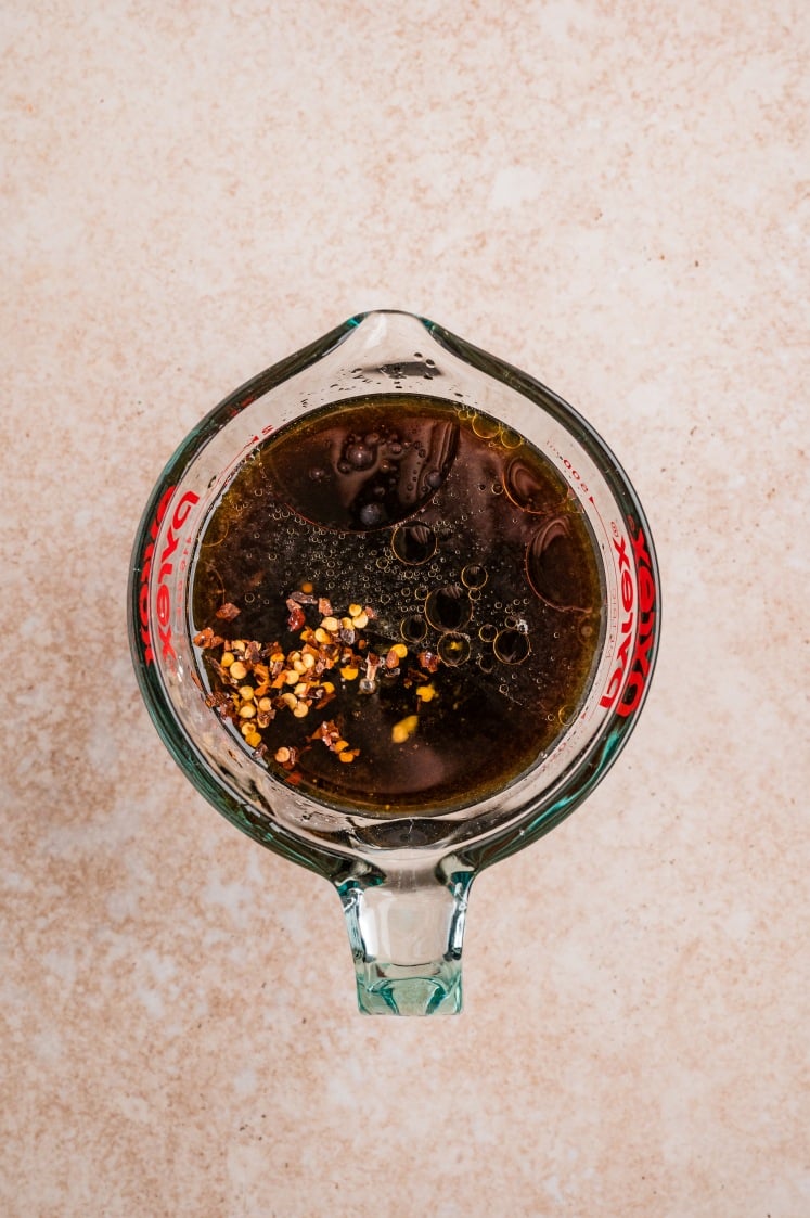 Measuring cup with soy-based sauce, oil, and red chili flakes.