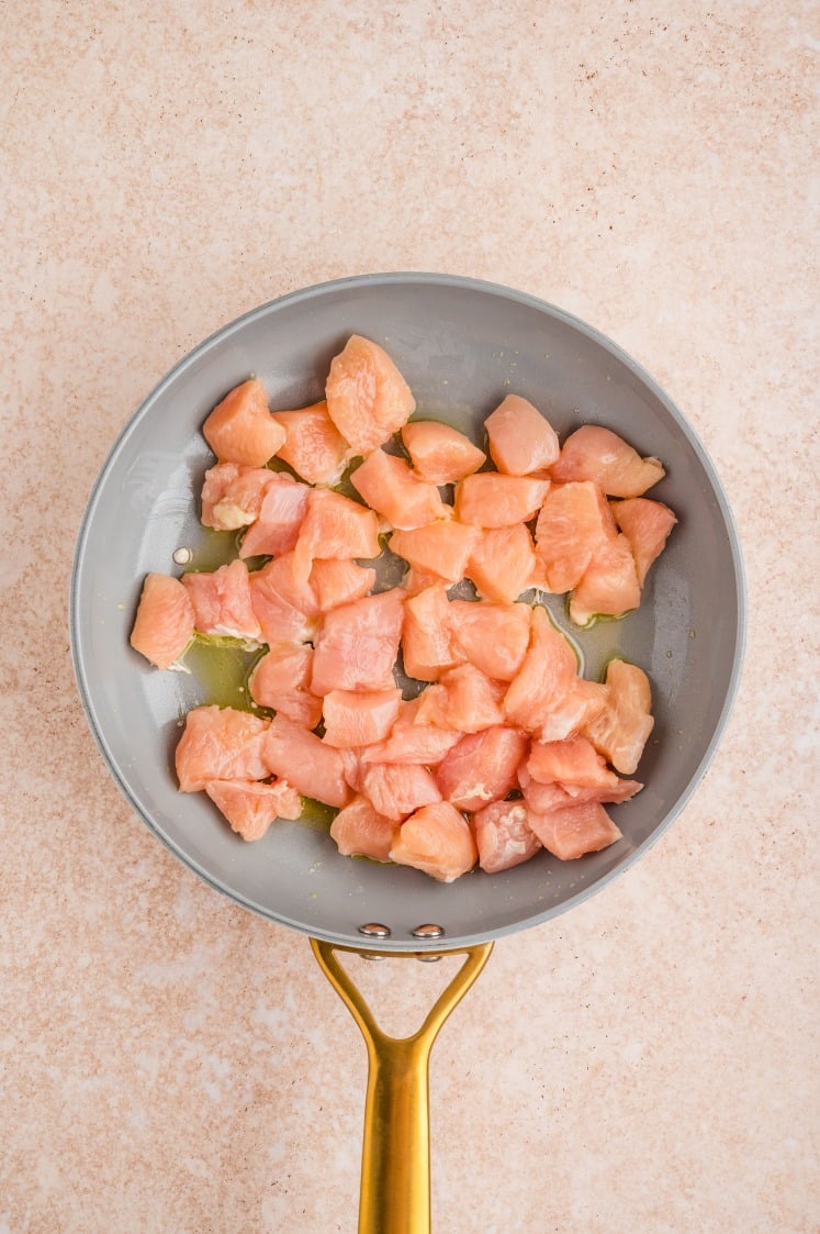 Diced chicken cooking in a skillet with oil.