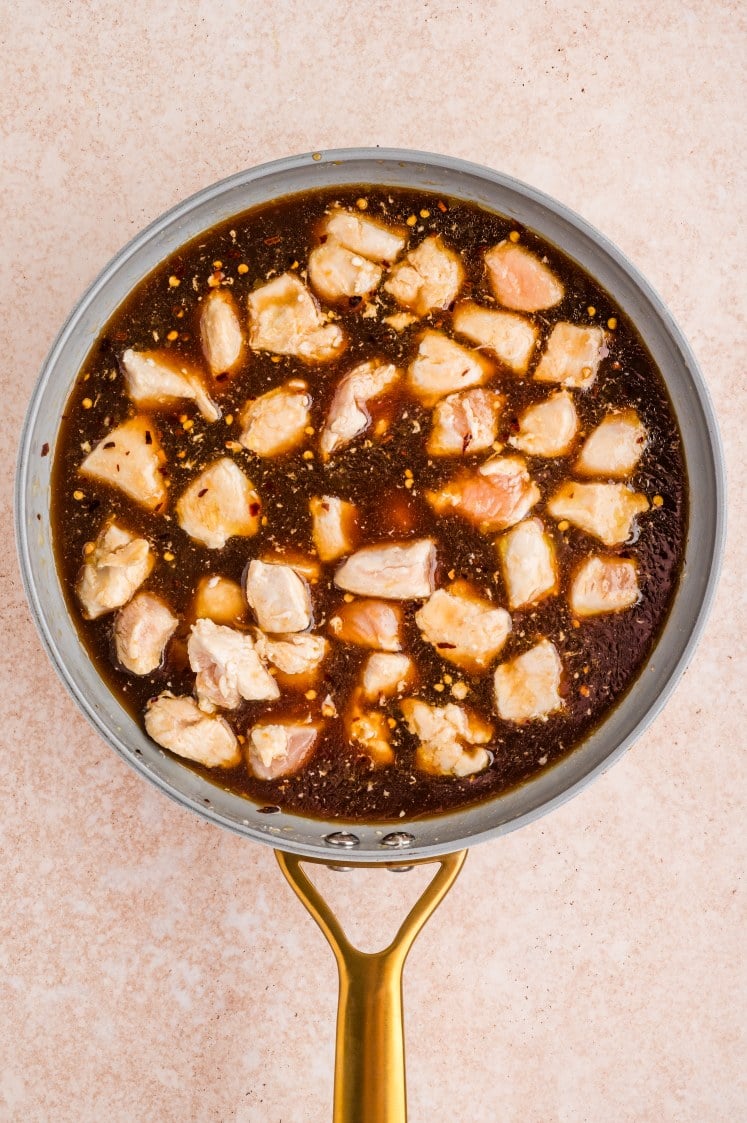 Chicken simmering in dark soy-based sauce in a skillet.
