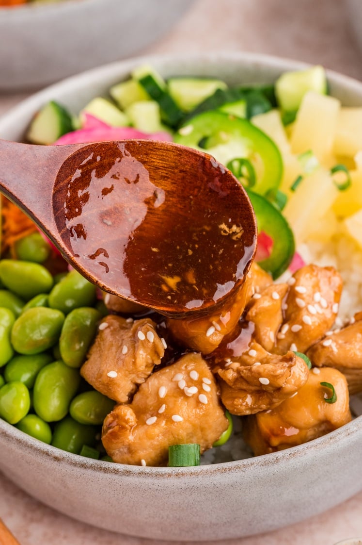 Sauce spoon drizzling over chicken in a poke bowl.