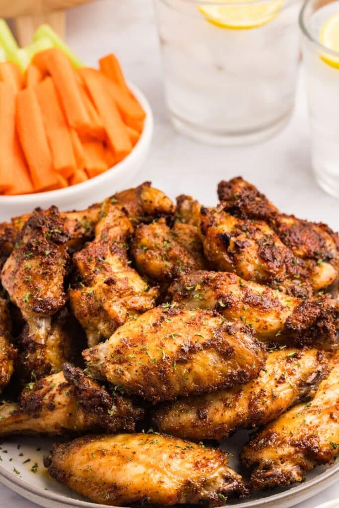 Crispy spice rubbed chicken wings piled on a plate with carrot sticks and lemon drinks.