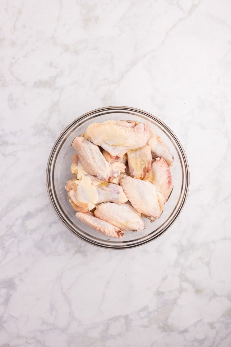 Bowl of raw chicken in a glass dish on a white marble surface.