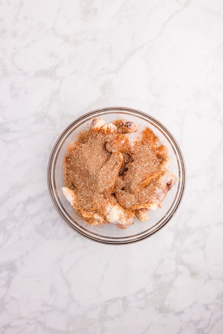 Raw chicken wings coated with dry spice rub in a glass bowl.