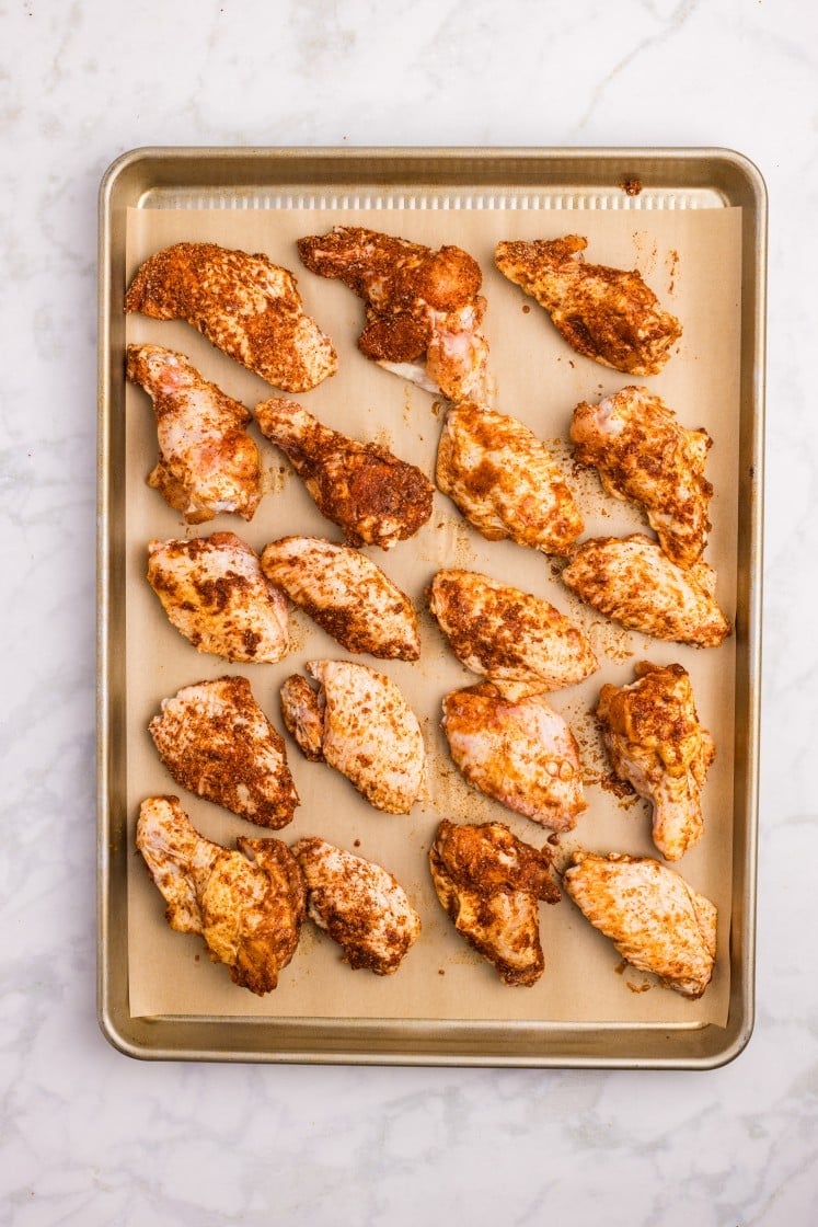 Seasoned chicken wings arranged on a parchment-lined baking sheet.