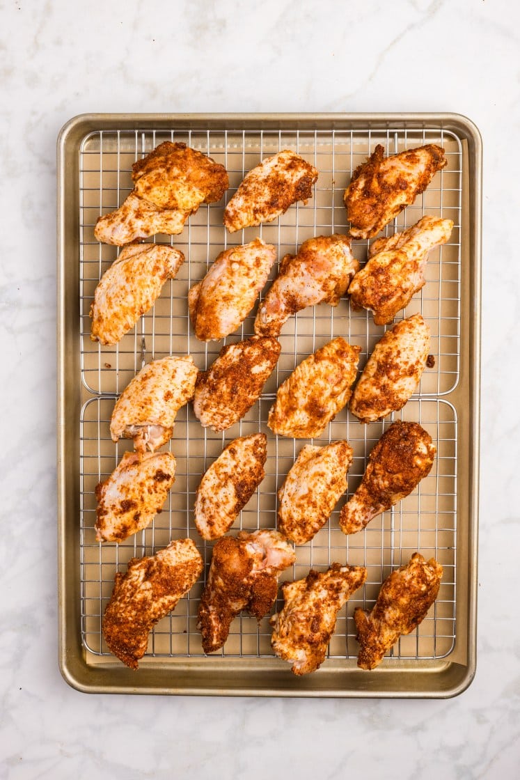 Spice-rubbed chicken wings spaced on a wire rack over a baking sheet.