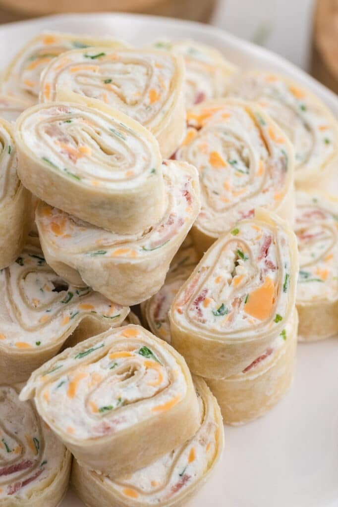 Close-up of stacked chicken bacon ranch pinwheel slices showing the cream cheese and cheddar filling on a white plate.
