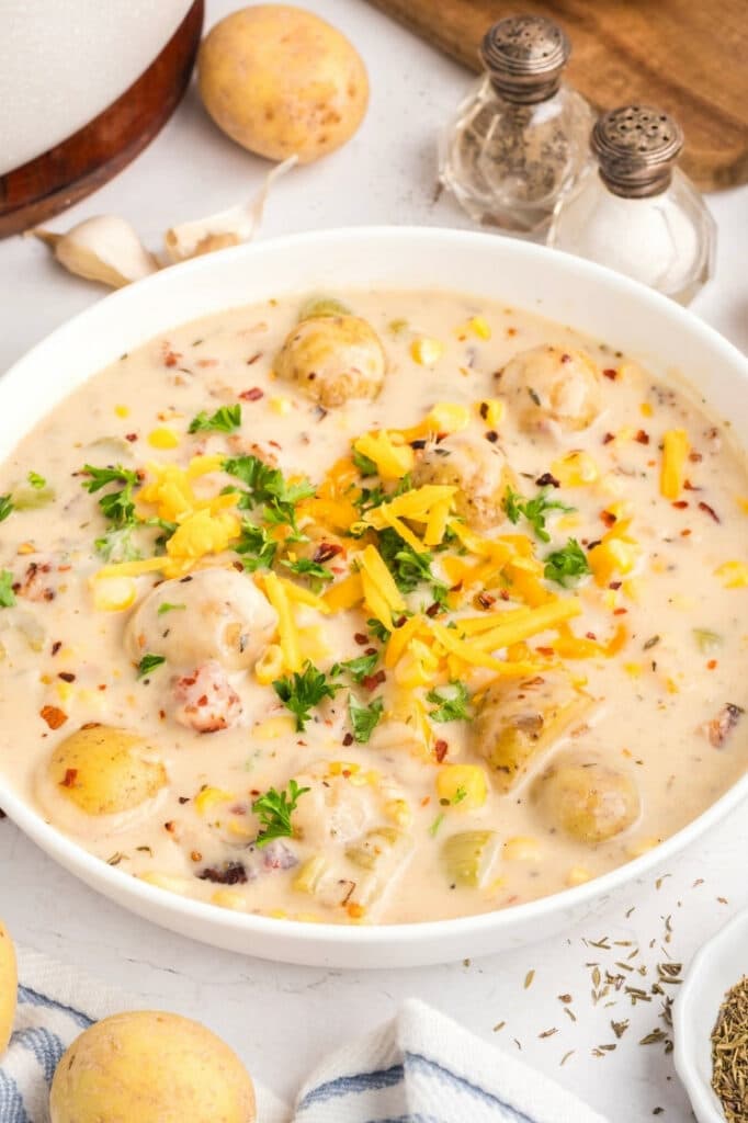 Overhead view of a white bowl of corn and potato chowder topped with shredded cheddar, parsley, and red pepper flakes.
