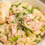 Close-up of creamy salmon orzo in a bowl, showing flaky salmon, peas, asparagus, and orzo coated in a creamy sauce with herbs and cheese.
