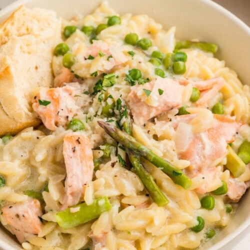 Close-up of creamy salmon orzo in a bowl, showing flaky salmon, peas, asparagus, and orzo coated in a creamy sauce with herbs and cheese.