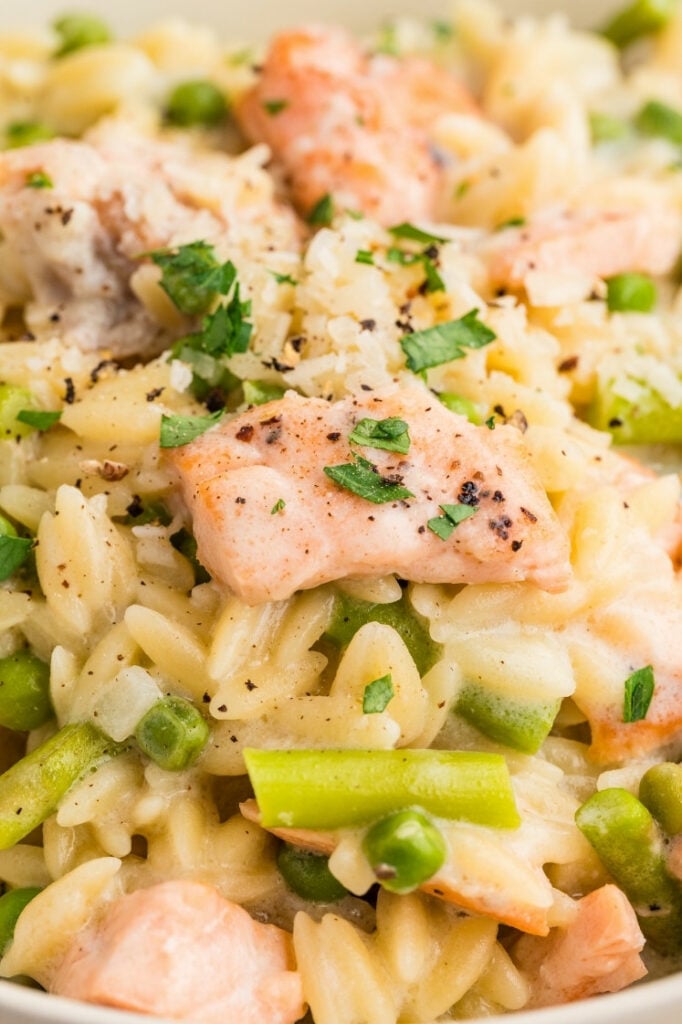 Close-up of creamy salmon orzo highlighting flaky salmon, peas, and asparagus mixed into a creamy, herb-flecked sauce.