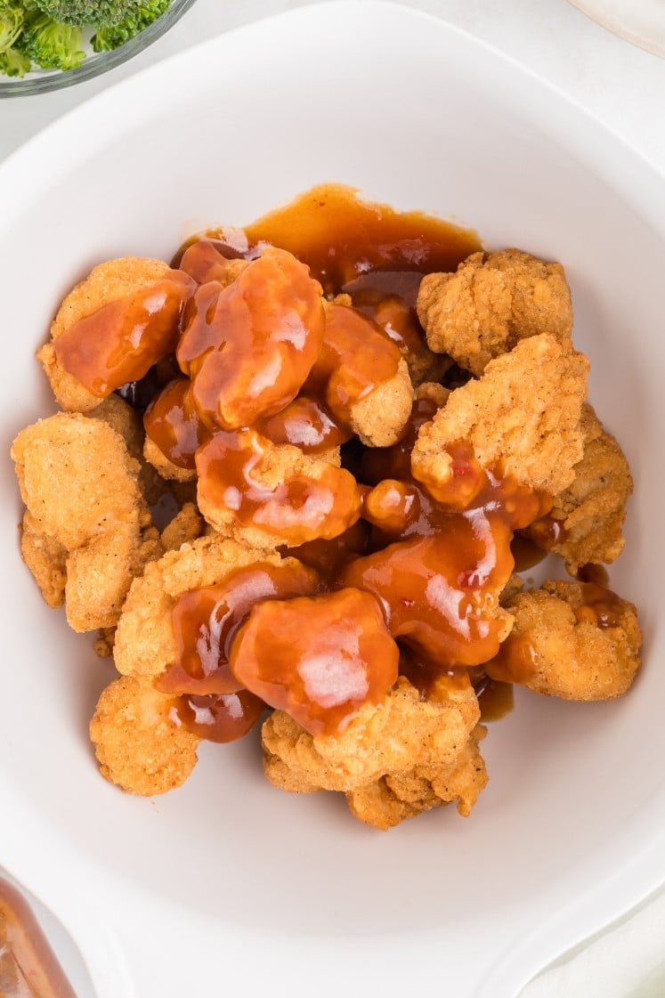 Overhead view of crispy fried chicken pieces in a bowl, partially coated in glossy General Tso’s sauce, showing the contrast between crunchy coating and sticky glaze.